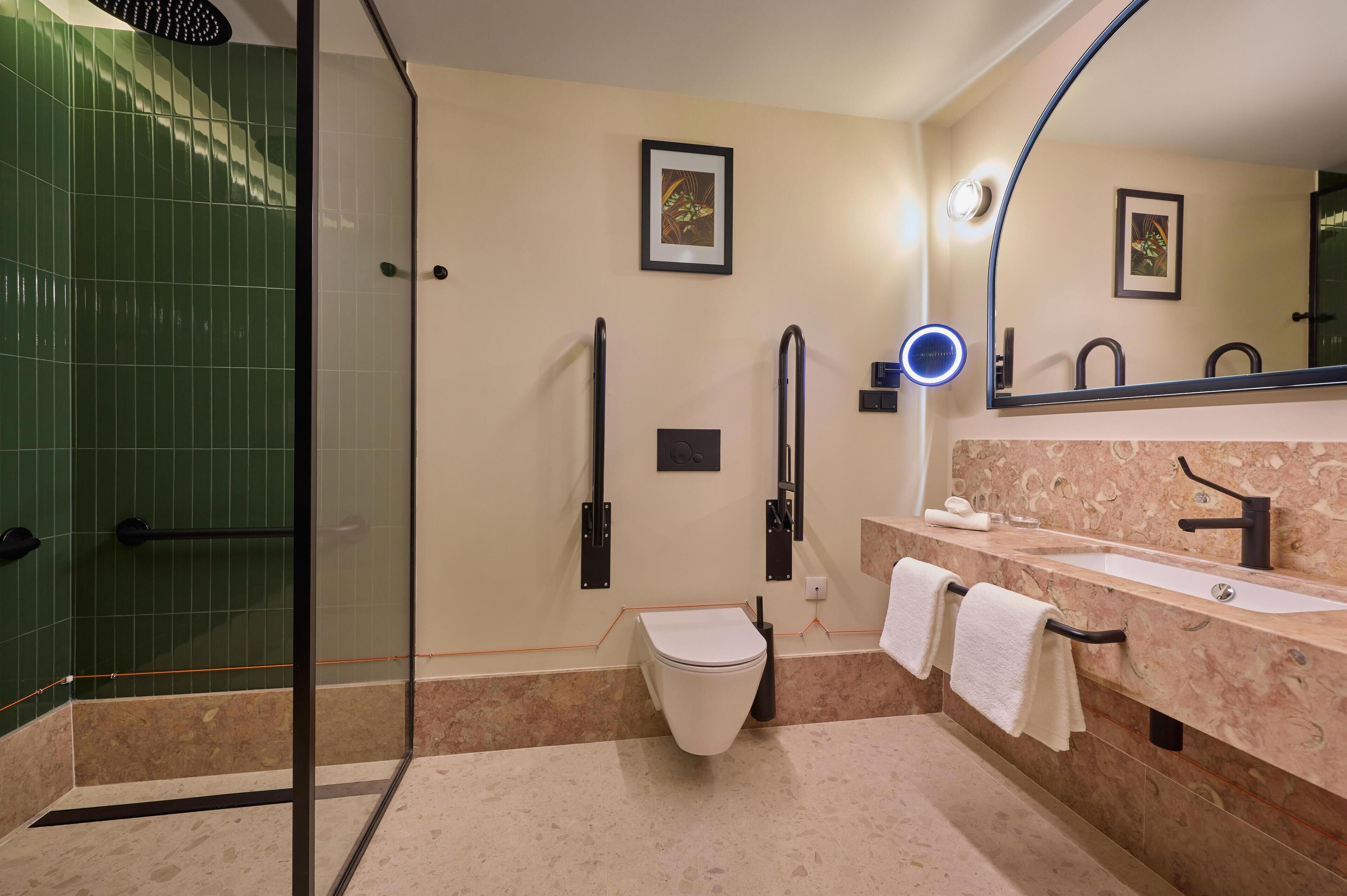 A modern bathroom with a glass shower enclosure, a toilet, a sink with a marble countertop, and two framed pictures on the wall.