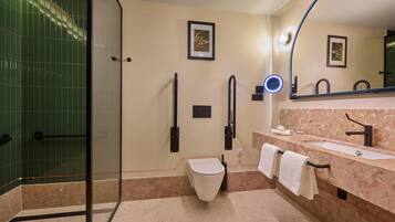 A modern bathroom with a glass shower enclosure, a toilet, a sink with a marble countertop, and two framed pictures on the wall.