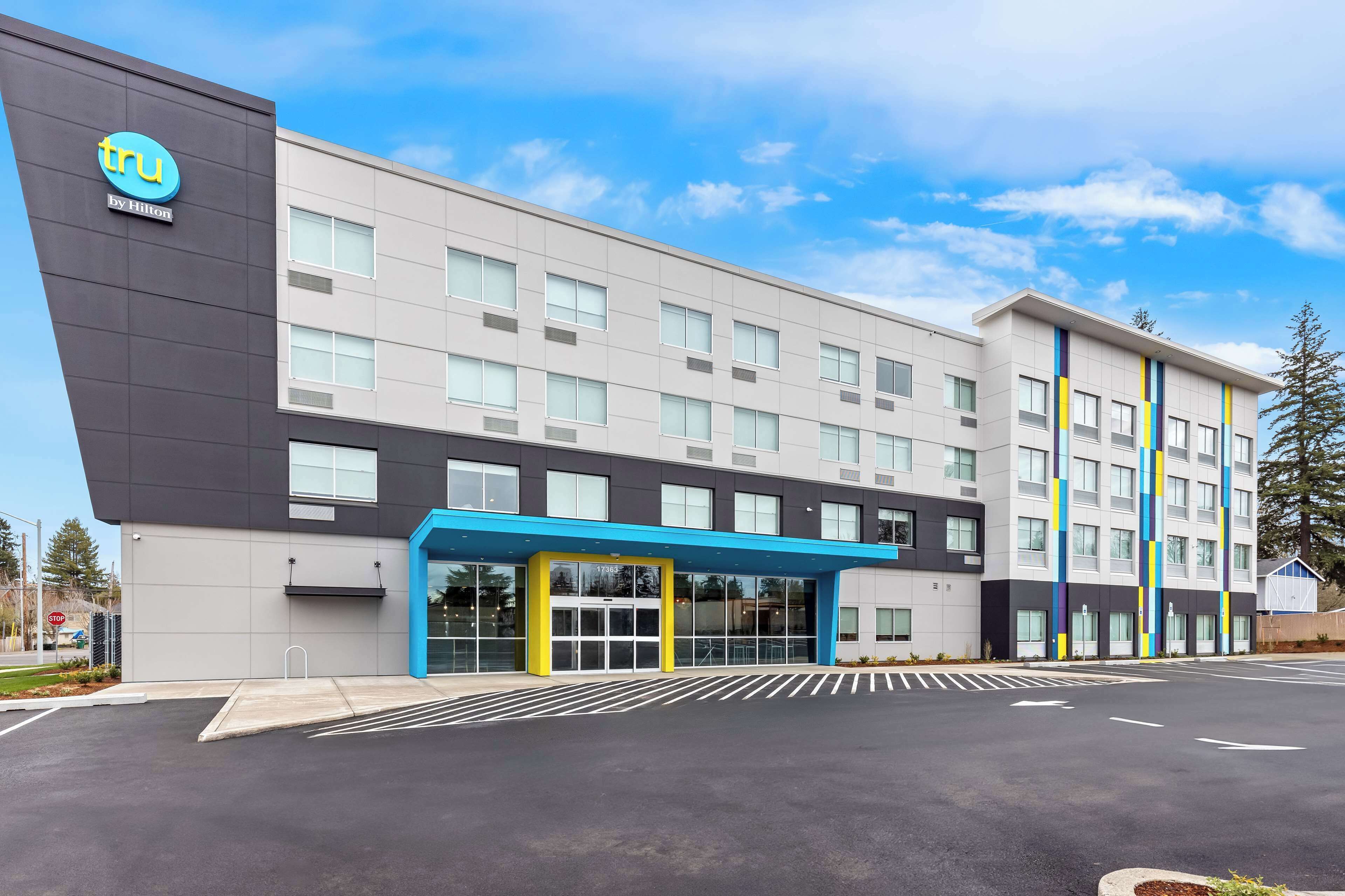 A modern hotel with a blue and white facade, a covered entrance, and a parking lot.