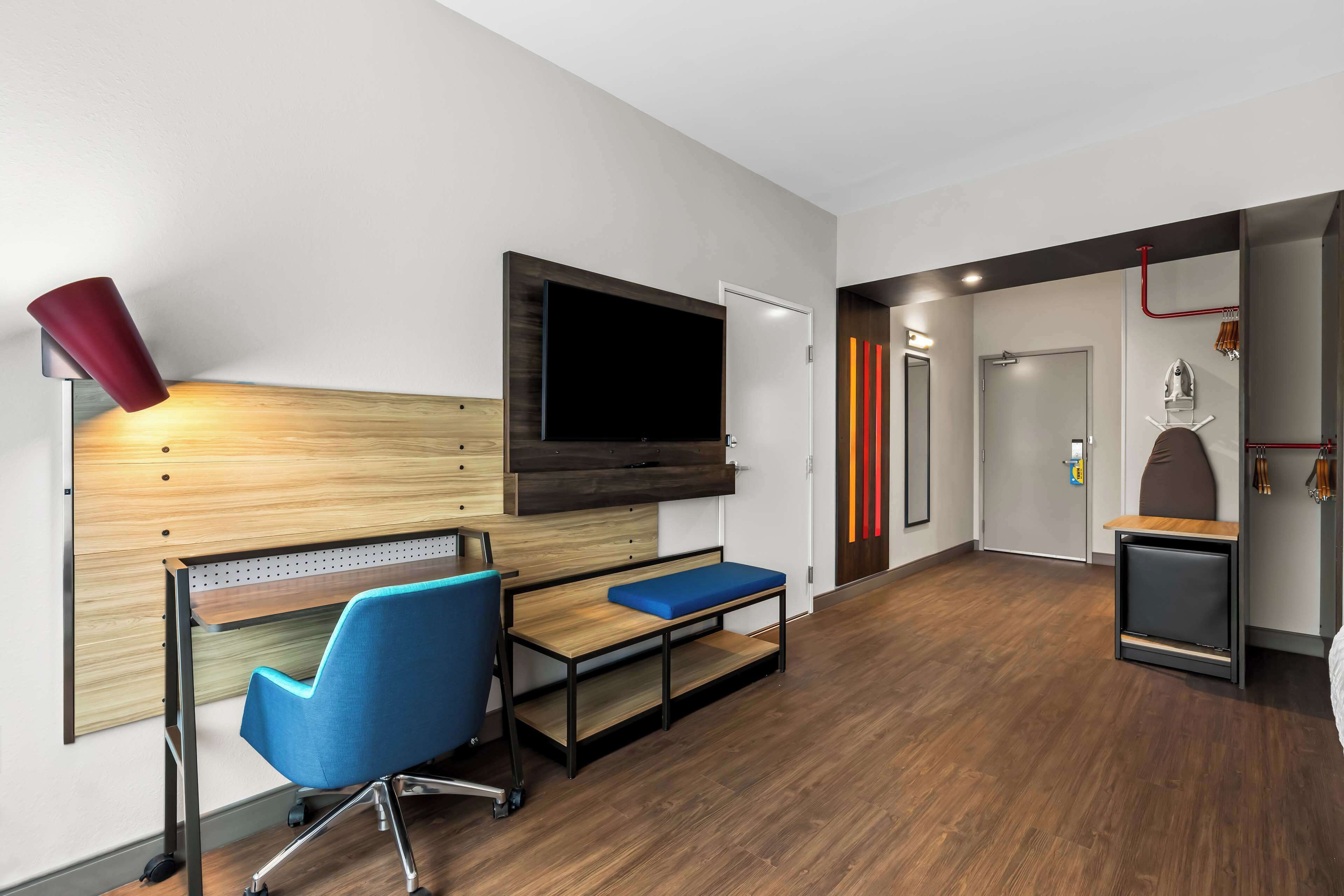 Una habitación moderna con un escritorio de madera, una silla azul y un televisor montado en la pared.