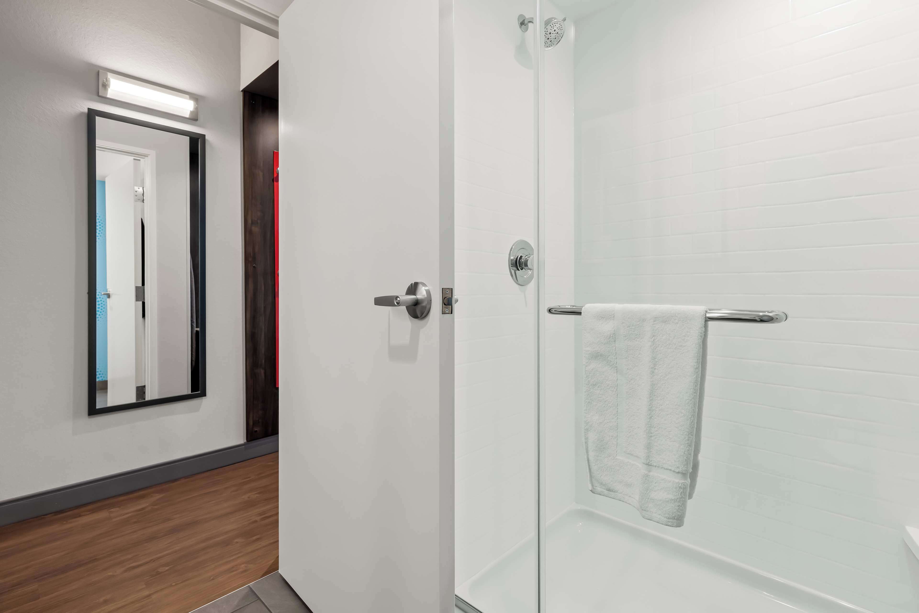 A modern bathroom with a glass shower enclosure, a white towel hanging on the wall, and a mirror reflecting the room.