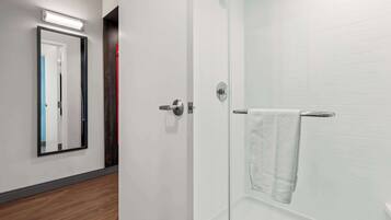A modern bathroom with a glass shower enclosure, a white towel hanging on the wall, and a mirror reflecting the room.