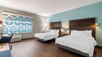 Een hotelkamer met twee bedden, een bureau en een raam met een geometrisch patroon.