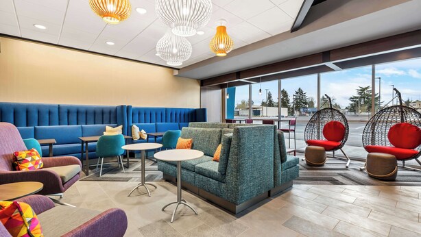 A modern lounge area with seating options including sofas, chairs, and a hanging chair, with large windows providing a view of the outdoors. - Tru By Hilton Aloha Beaverton (Aloha)