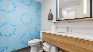 A bathroom with a blue patterned wall, a white toilet, a wooden vanity with a mirror, and a towel rack.