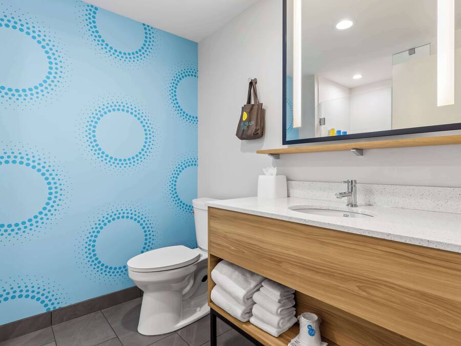 A bathroom with a blue patterned wall, a white toilet, a wooden vanity with a mirror, and a towel rack.