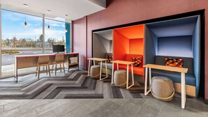 A modern interior with a seating area, a desk with chairs, and a large window offering a view of the outside. - Tru By Hilton Aloha Beaverton (Aloha)