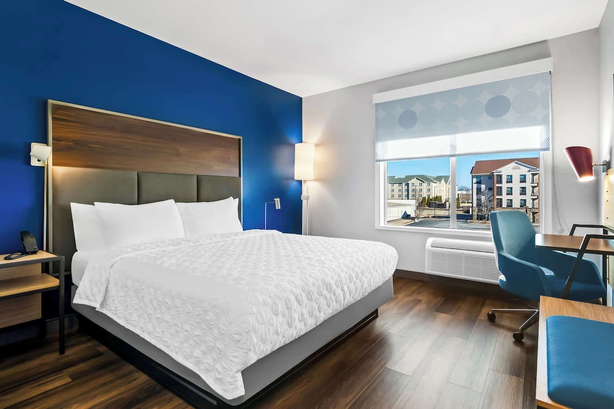 A hotel room with a large bed, a desk, a chair, and a window with a view of buildings.