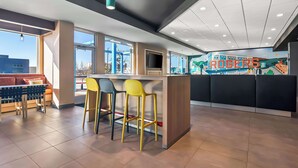 A modern bar area with a counter, bar stools, and a television screen. - Tru By Hilton Rogers Bentonville (Rogers)
