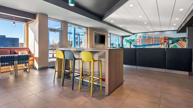 A modern bar area with a counter, bar stools, and a television screen. - Tru By Hilton Rogers Bentonville (Rogers)