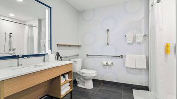 A modern bathroom with a white sink, toilet, and shower area. There are handrails and a towel rack on the wall.