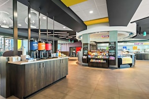 Interior de una cafetería moderna con barra de café, zona de estar y un puesto de aperitivos.