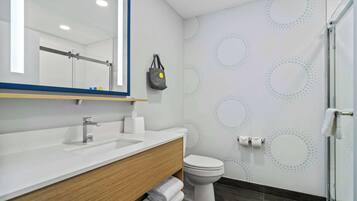 A modern bathroom with a white sink, wooden vanity, a toilet, and a shower area.