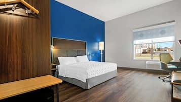 A modern hotel room with a large bed, a desk, and a view of the outside.