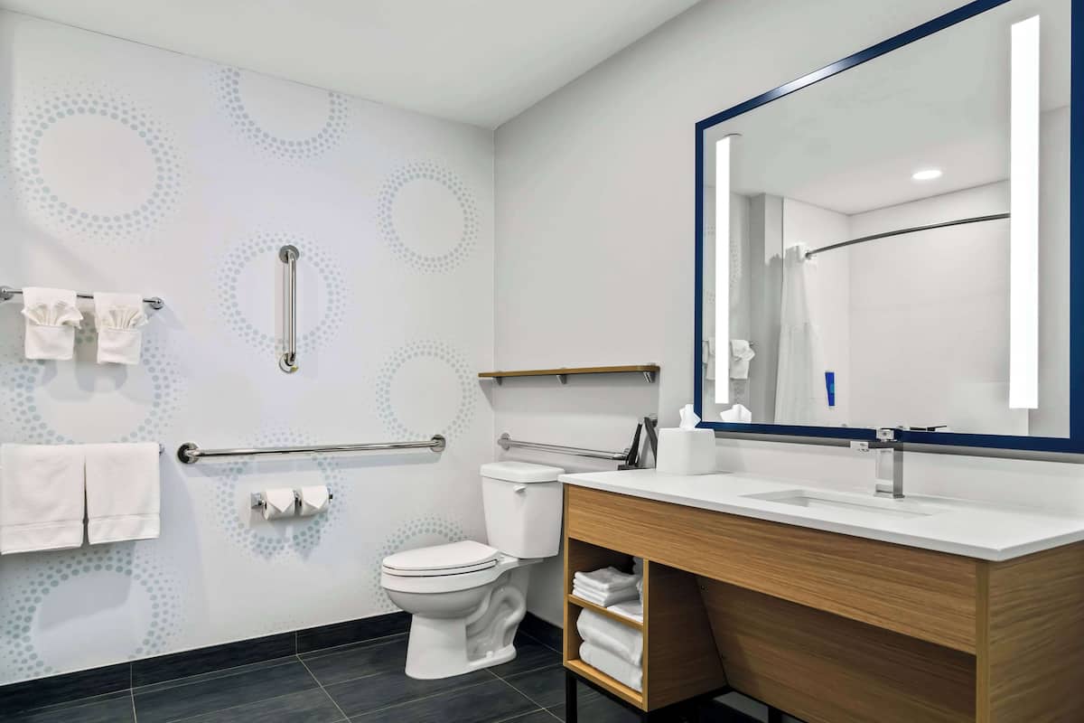 A modern bathroom with a white toilet, a large mirror, and a wooden vanity.