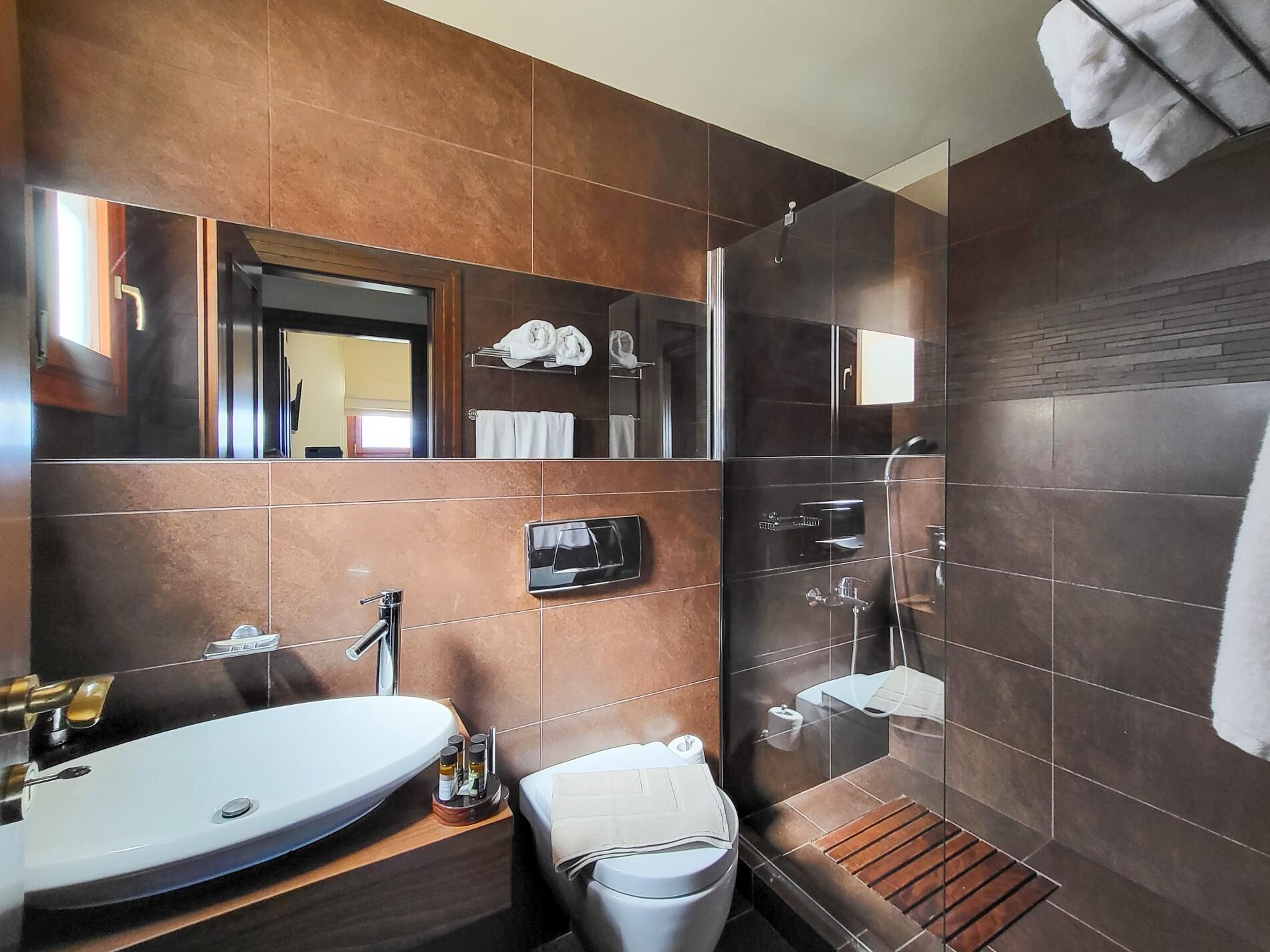 A modern bathroom with a large mirror, a sink, a shower, and a toilet.