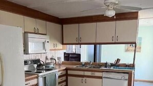 Une cuisine de taille réduite, avec des meubles blancs, un four à micro-ondes, une cuisinière et un lave-vaisselle.
