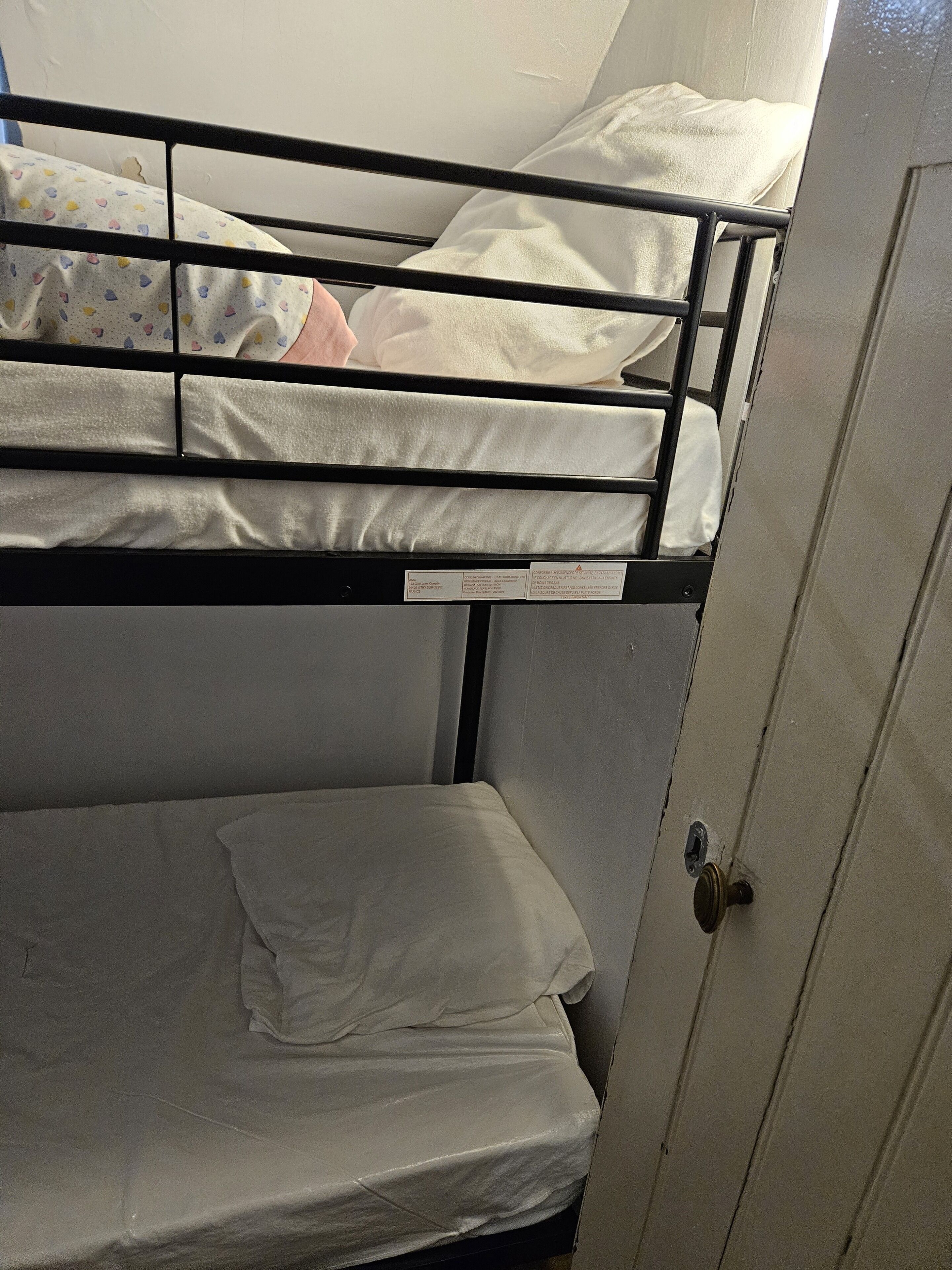 A bunk bed with a white mattress and a single pillow. There is a door with a handle on the right side.