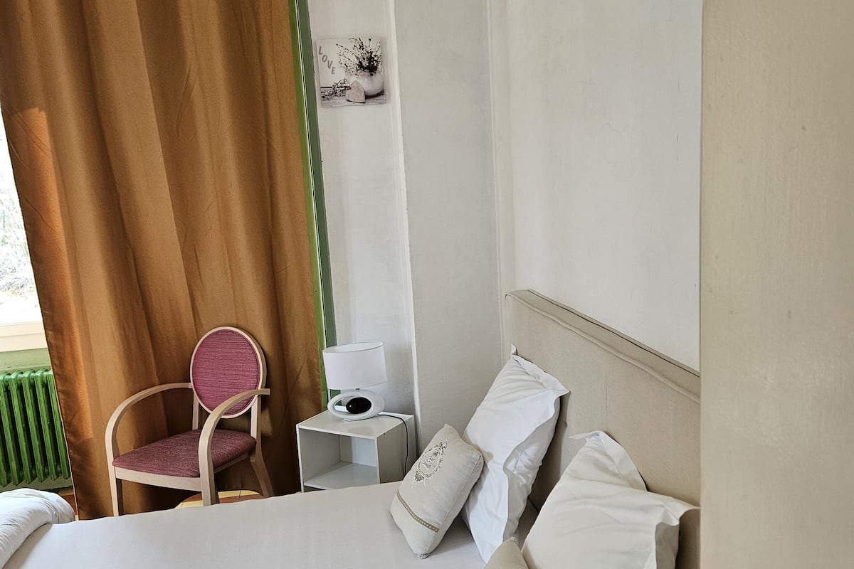 A hotel room with a bed, a chair, a nightstand with a lamp, and a wall with a picture.