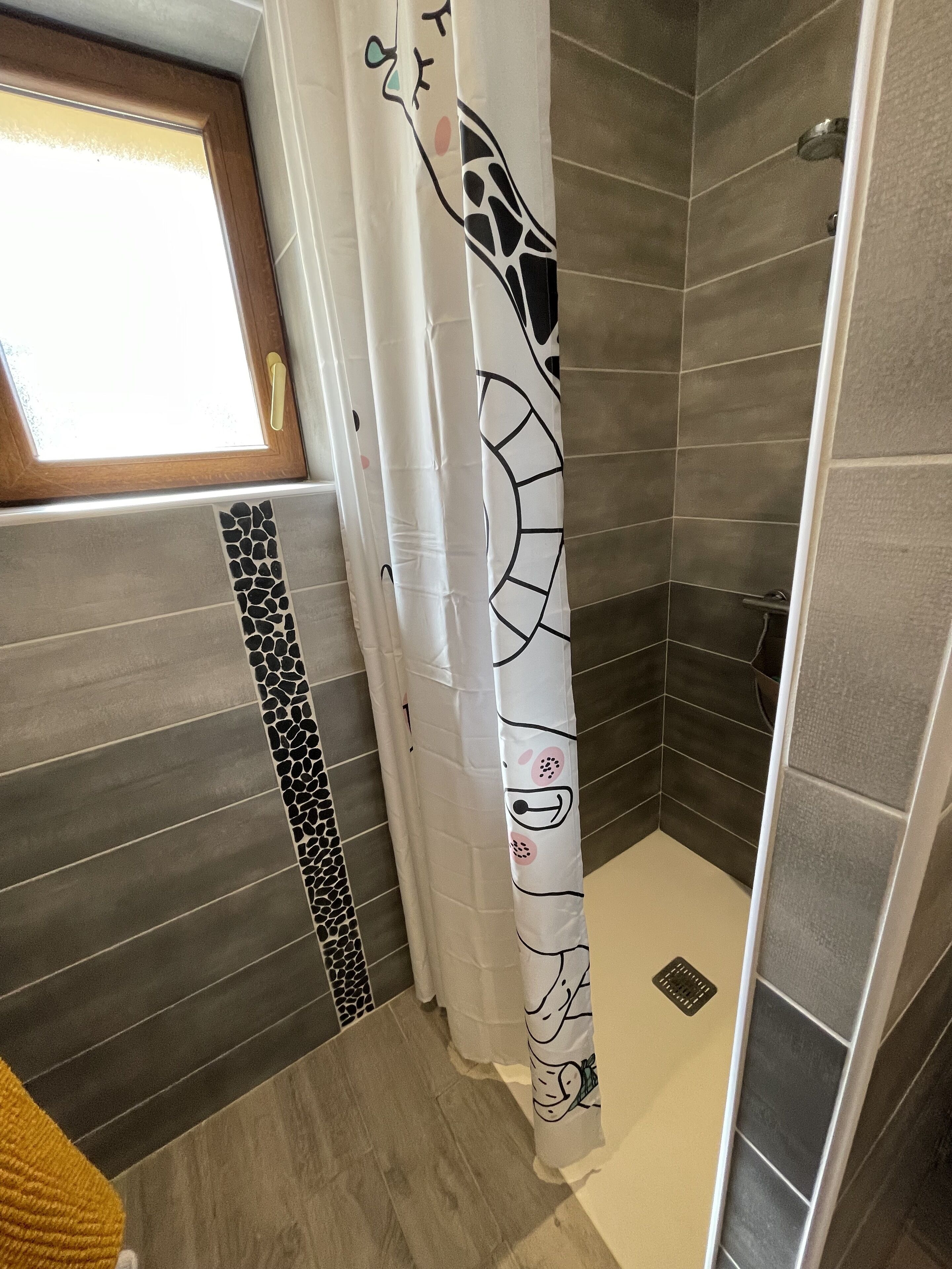 A bathroom with a shower curtain featuring a giraffe design, tiled walls, and a wooden-framed window.