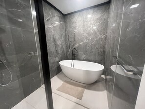 A modern bathroom with a freestanding bathtub, a glass shower enclosure, and marble walls.