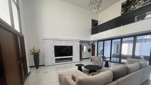 Un salon moderne doté d’un grand canapé d’angle, d’un téléviseur à écran plat, d’une cheminée en marbre et d’un balcon avec de grandes fenêtres.