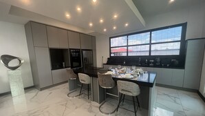 Une cuisine moderne avec un sol en marbre, des appareils électroménagers intégrés et un coin repas doté de tabourets de bar.