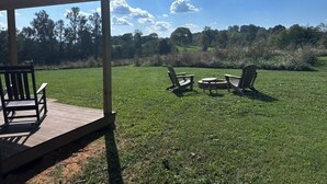 Un espacio al aire libre cubierto con piso de madera, dos sillas Adirondack y una mesita.