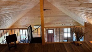 Amplia habitación en el ático con vigas de madera, una escalera y ventanas grandes.