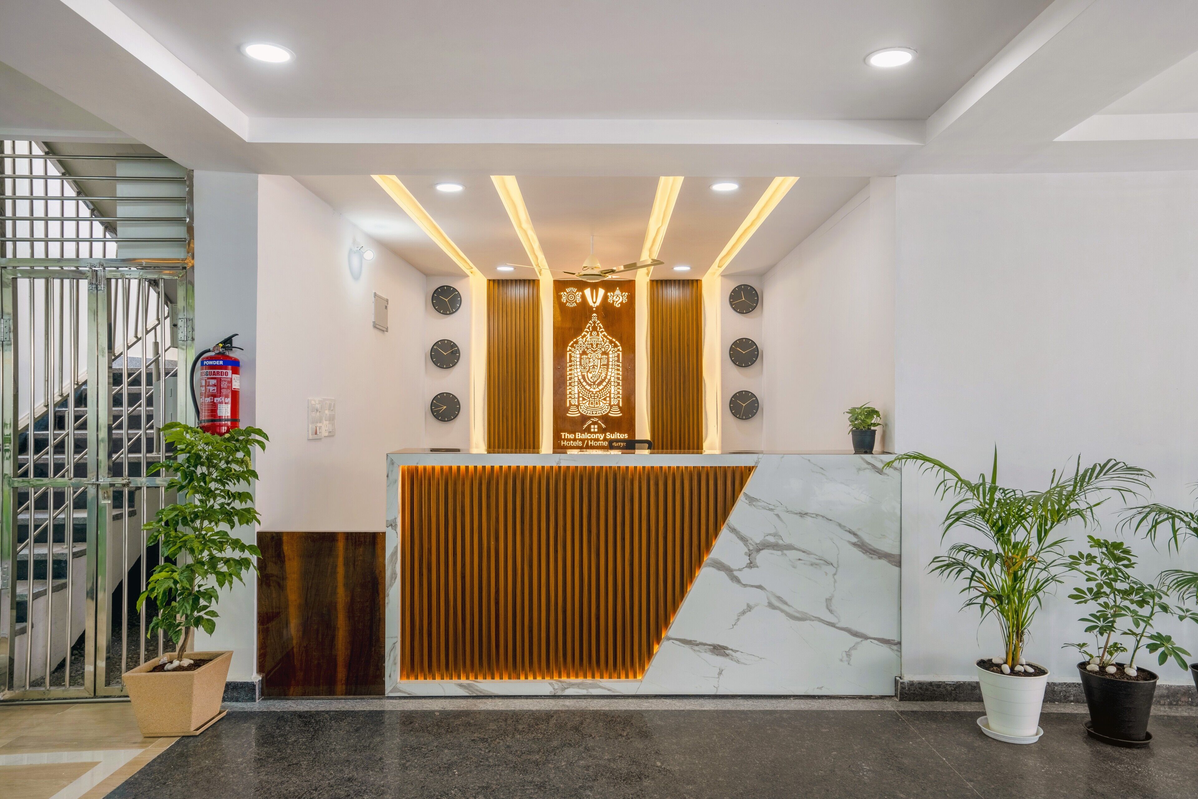 A hotel reception area with a modern design, featuring a reception desk, a clock, and a staircase.