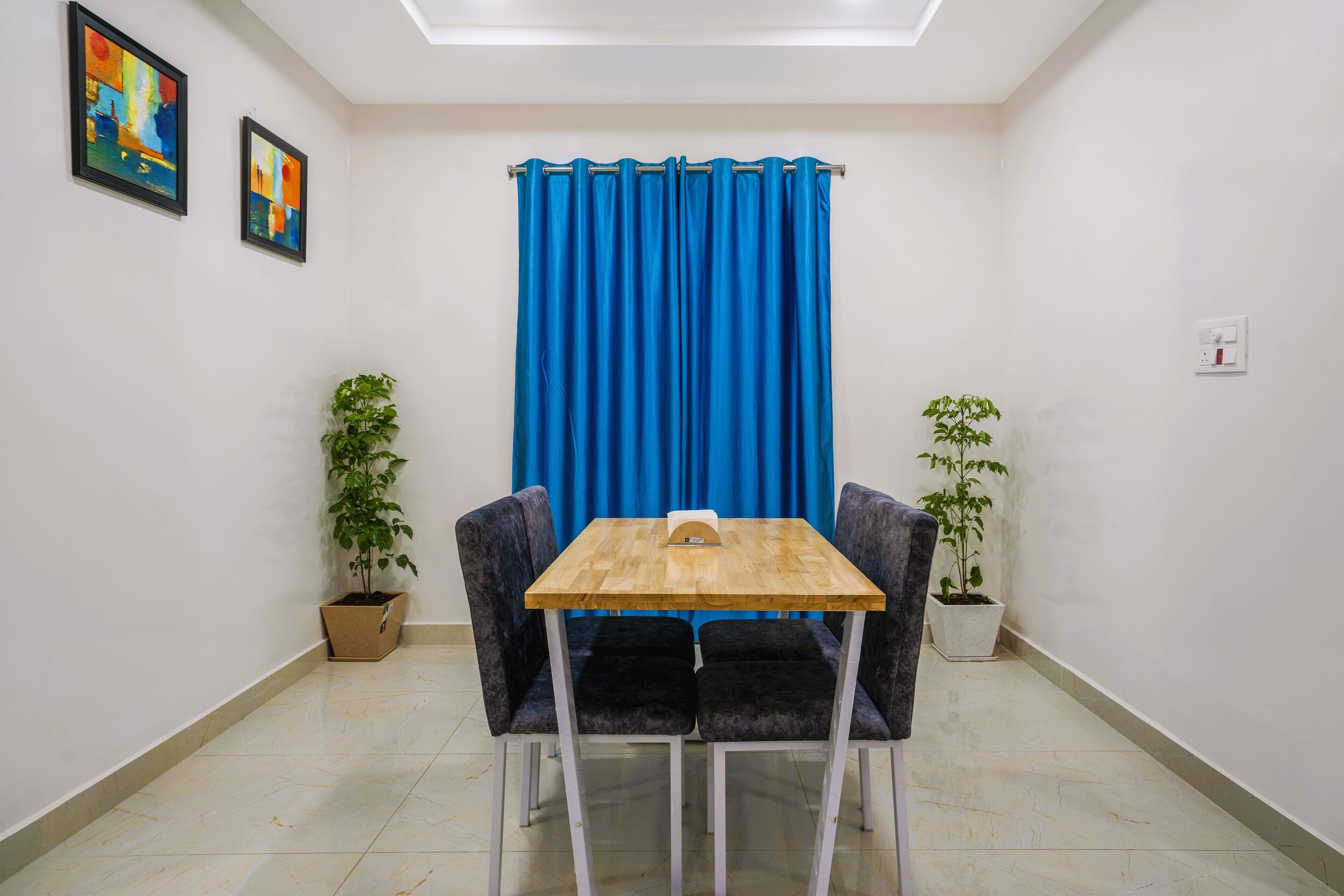 A small room with a wooden table and two chairs, a blue curtain, and two potted plants.