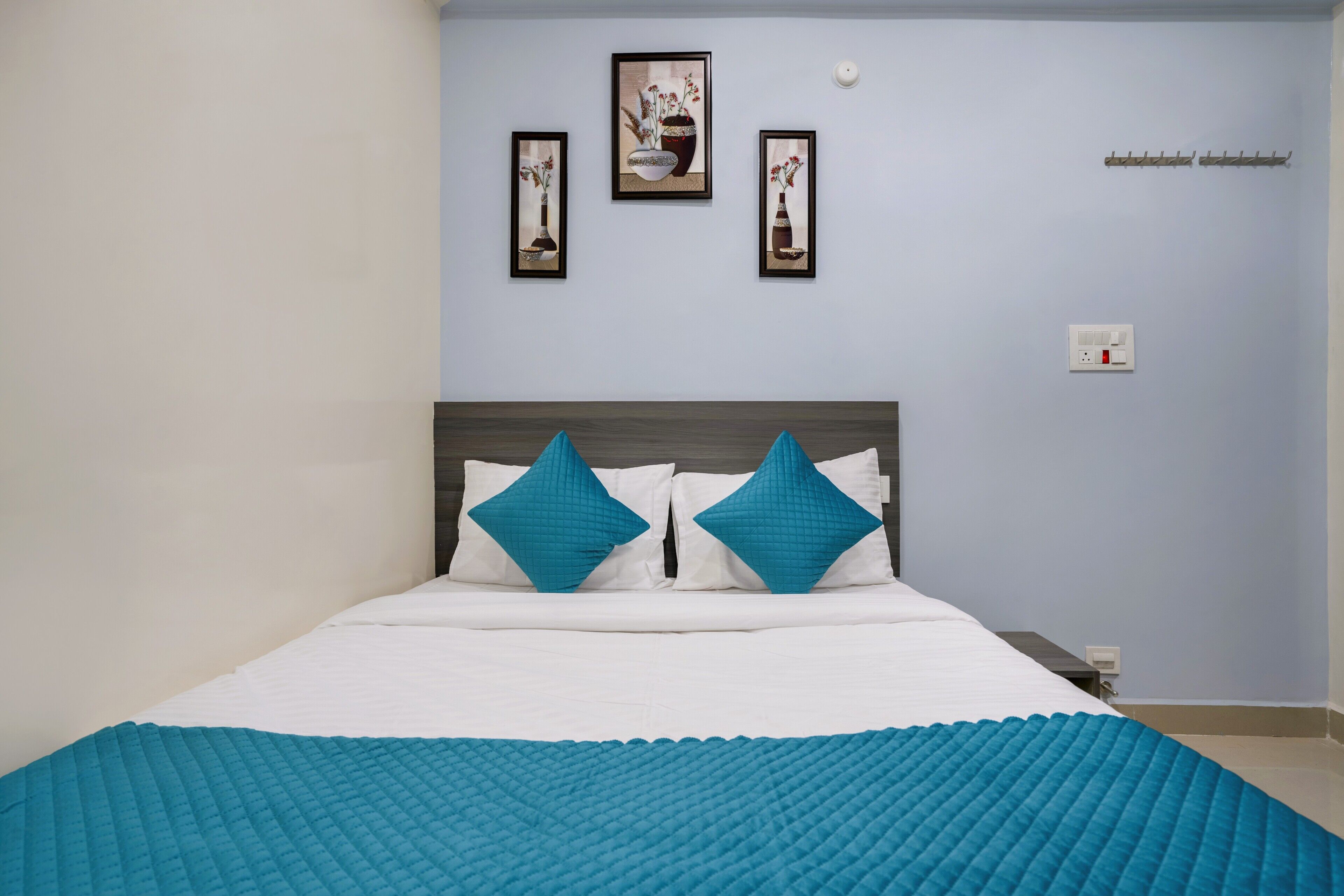A neatly made bed with white and teal bedding, two teal pillows, and a teal quilted blanket. There are three framed artworks on the wall above the bed.