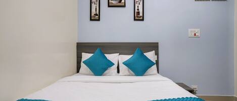 A neatly made bed with white and teal bedding, two teal pillows, and a teal quilted blanket. There are three framed artworks on the wall above the bed.