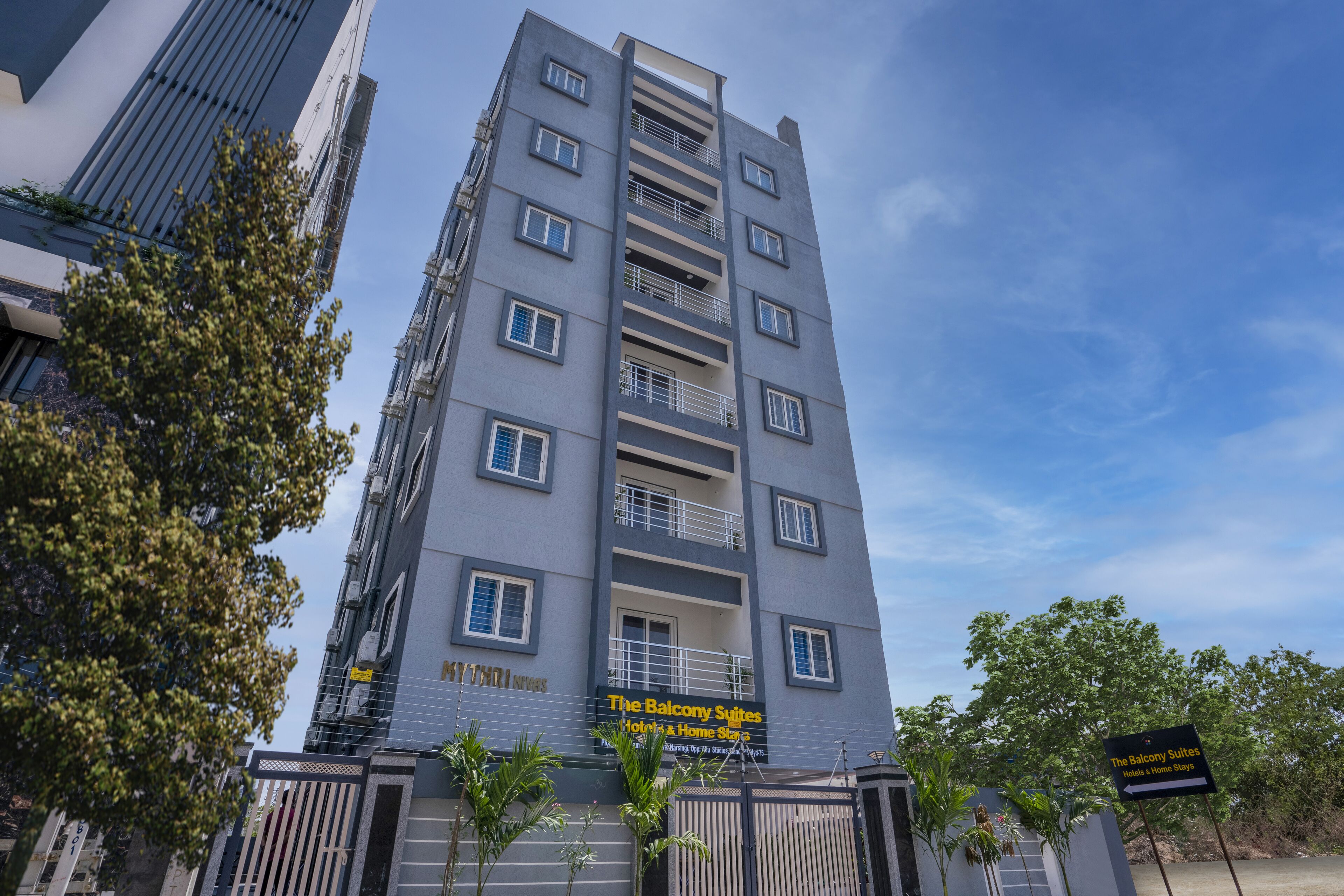 A multi-story hotel with balconies, a sign for 'The Balcony Suites', and a gated entrance.