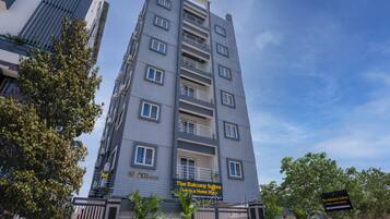 Un hôtel à plusieurs étages doté de balcons, une enseigne indiquant « The Balcony Suites », et une entrée sécurisée par un portail.