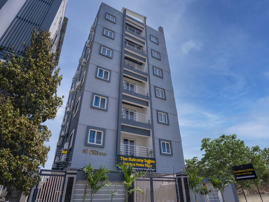 Un hôtel à plusieurs étages doté de balcons, une enseigne indiquant « The Balcony Suites », et une entrée sécurisée par un portail.