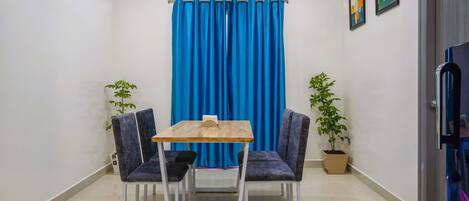 Una stanza con un tavolo da pranzo e sedie, una tenda blu e due piante in vaso.
