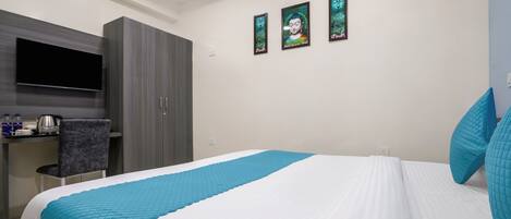 A hotel room with a bed, a desk with a flat-screen TV, and a wardrobe.