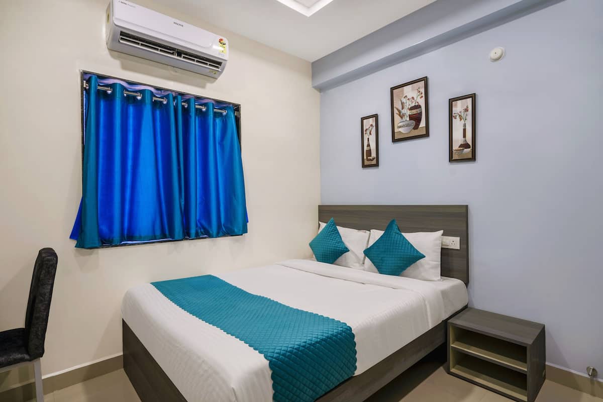 A hotel room with a bed, a chair, a nightstand, and a wall-mounted air conditioner.