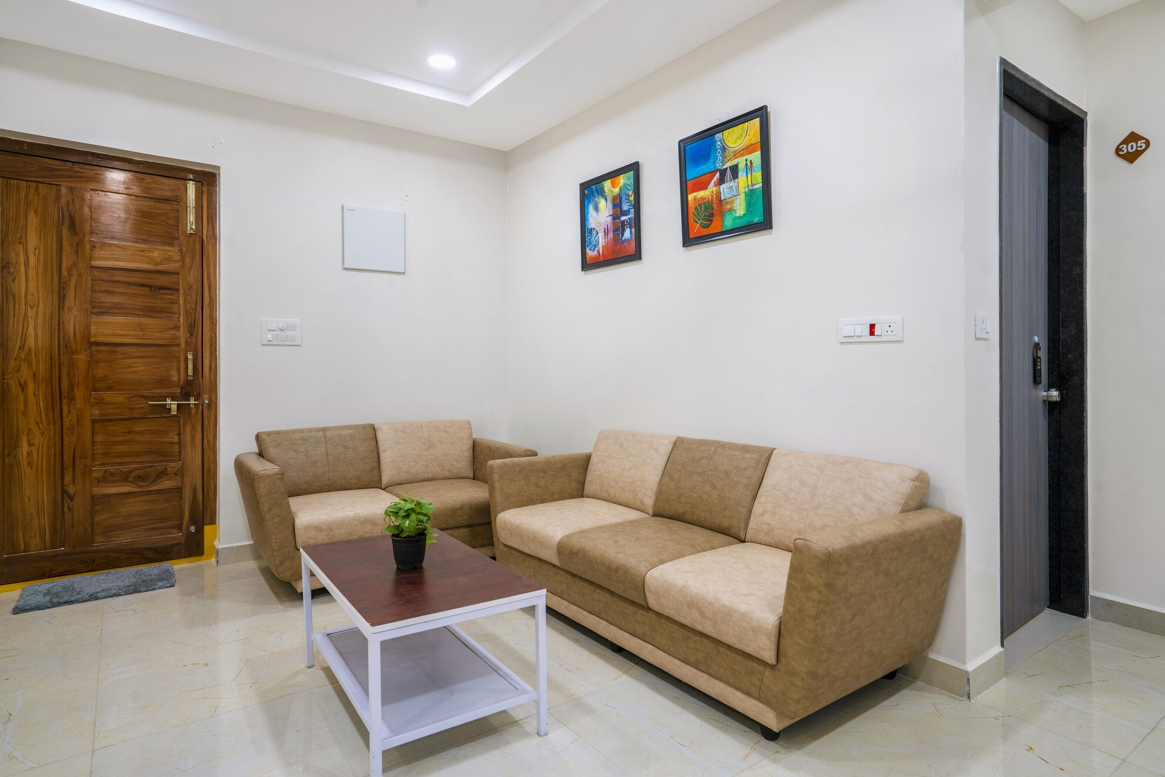 A living room with two beige sofas, a wooden door, and two framed artworks on the wall.