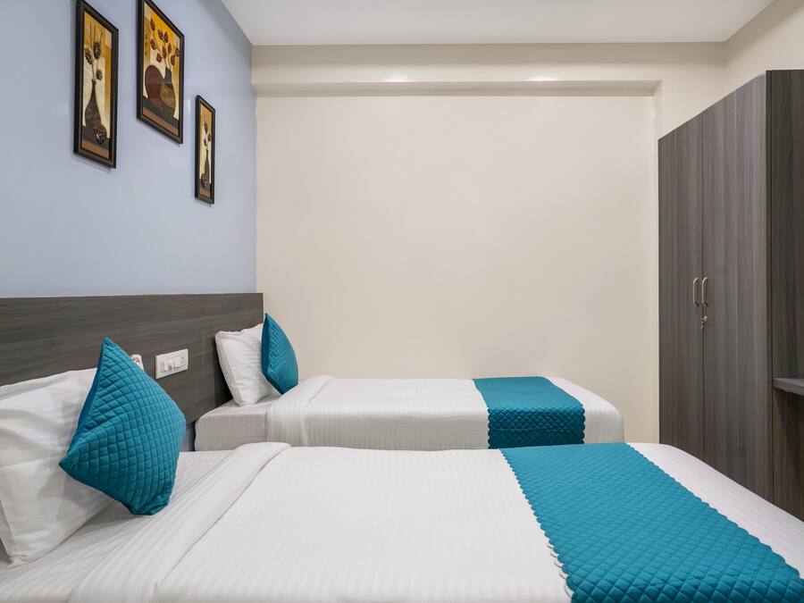 A hotel room with two beds, each with white bedding and teal accents, a wardrobe, and framed artwork on the wall.
