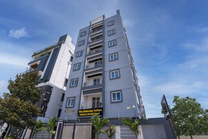 Monikerroksinen hotelli, jossa on parvekkeet. Kyltissä lukee ”The Balcony Suites”, mikä viittaa hotellin ja huoneistomajoituksen tarjontaan. Taustalla on kirkas, sininen taivas.