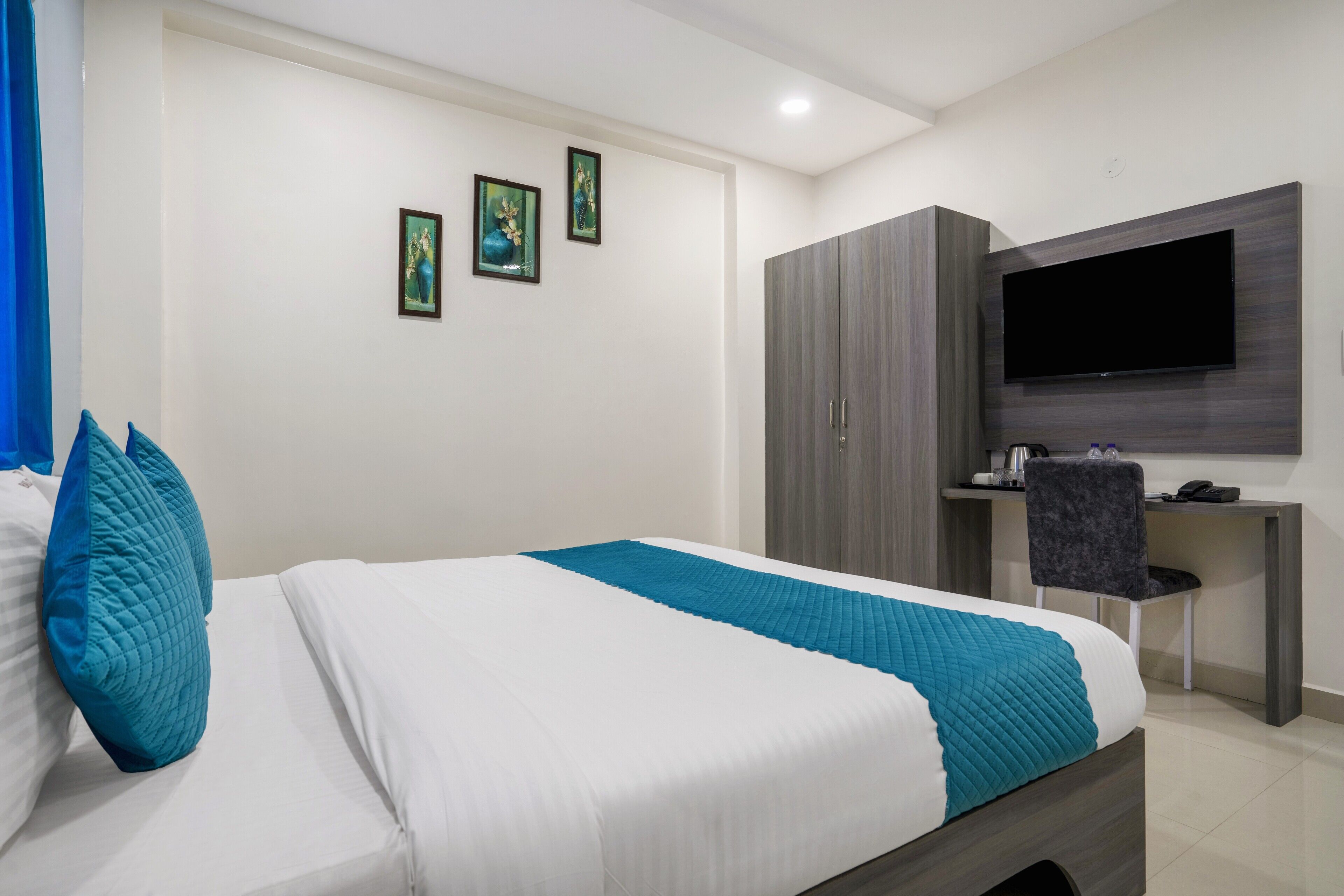 A modern hotel room with a bed, a desk, a TV, and artwork on the wall.