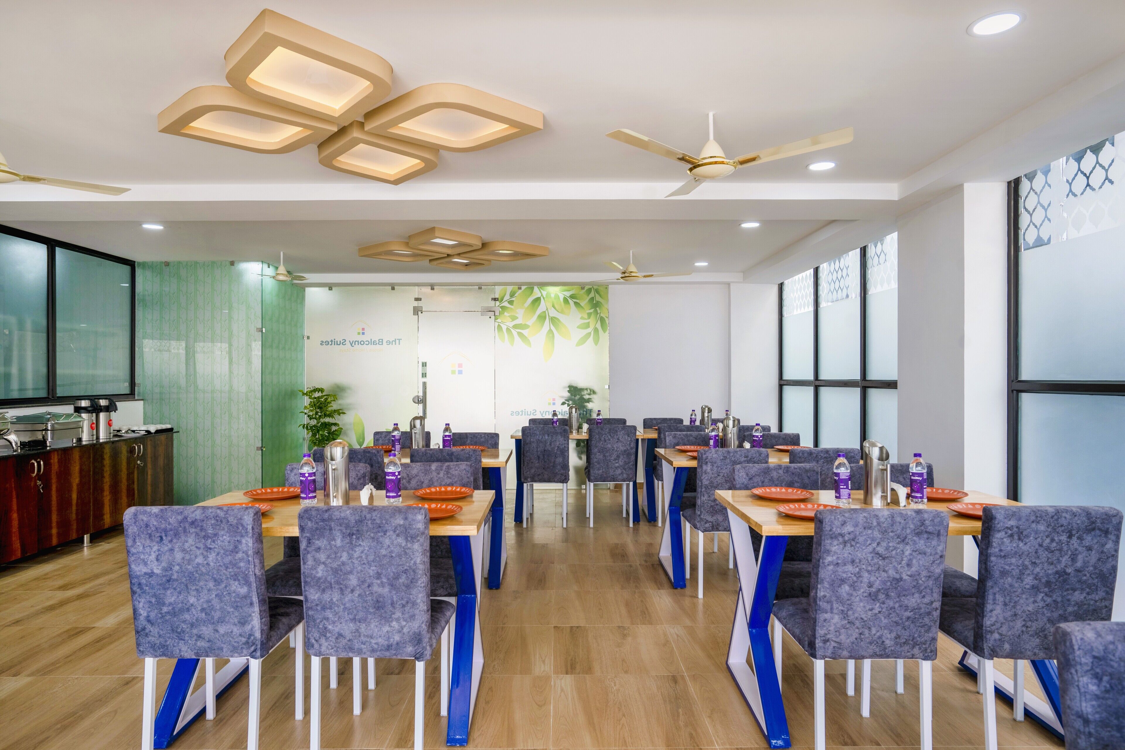 A conference room with multiple tables and chairs, ceiling fans, and a kitchen area with a refrigerator and stove.