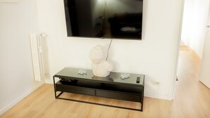 A modern living room with a mounted flat-screen TV, a glass-top coffee table with a sculpture, and a white radiator. - Wonderful Apartment near the Vatican and Historical Center (Roma)