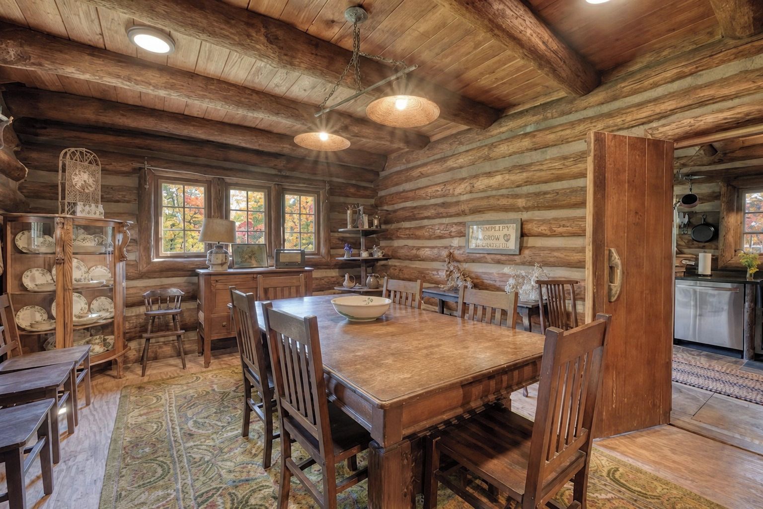 L’intérieur d’un chalet rustique comprend une table à manger en bois, des chaises, un lustre et un coin cuisine.