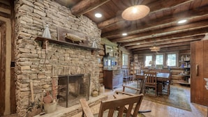 A rustic cabin interior with a stone fireplace, wooden dining table, and a cozy seating area. - Rustic Historical Cabin near Wineries & Gold Mines (Dahlonega)