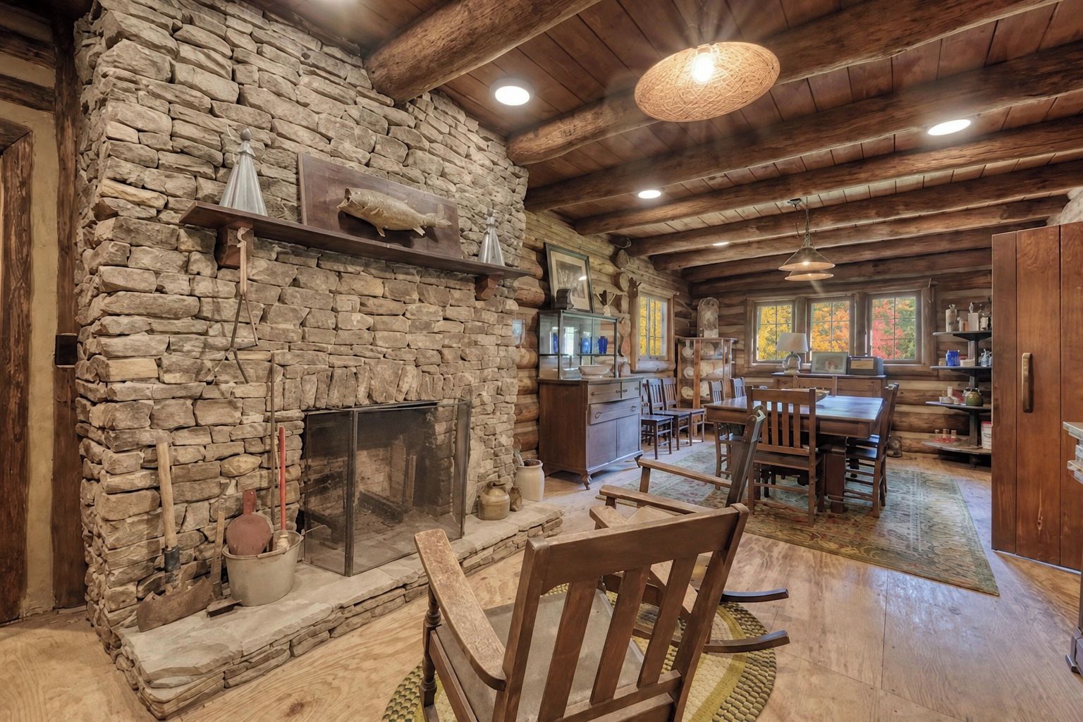 A rustic cabin interior with a stone fireplace, wooden dining table, and a cozy seating area.