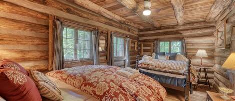 A log cabin bedroom with two beds, a wooden ceiling, and large windows.