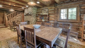 A rustic log cabin interior with a dining table, chairs, a stone fireplace, and a staircase. - Rustic Historical Cabin near Wineries & Gold Mines (Dahlonega)